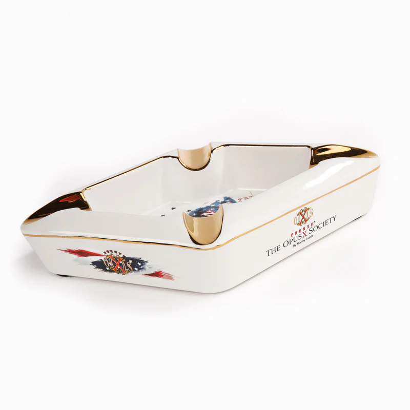 White ceramic ashtray with gold trim and a small crest/logo on the side, labeled The Opus Society (decorative/branded).
